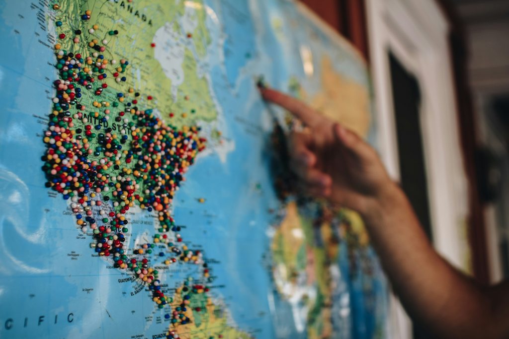 A hand pointing at a large world map covered in colorful pins